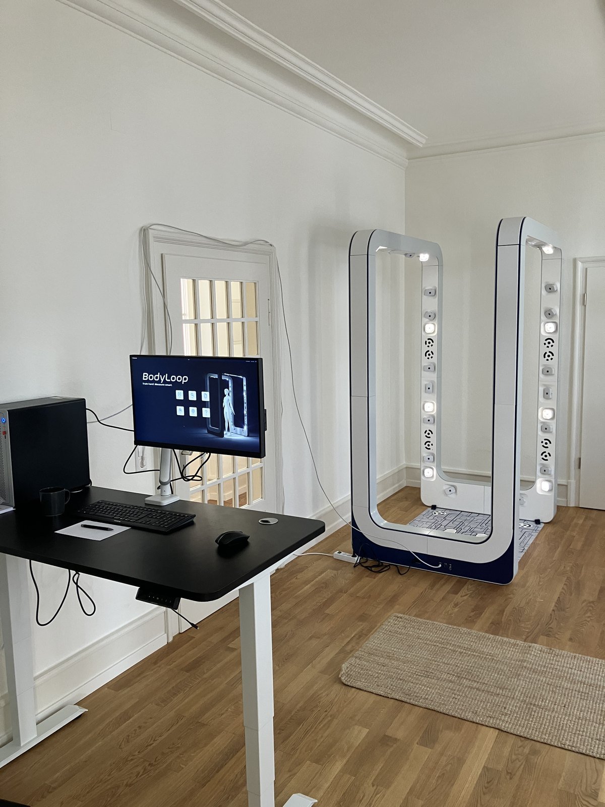 The BodyLoop scanner room: a white sensor arch on a floor mat beside a desk with the operator workstation.