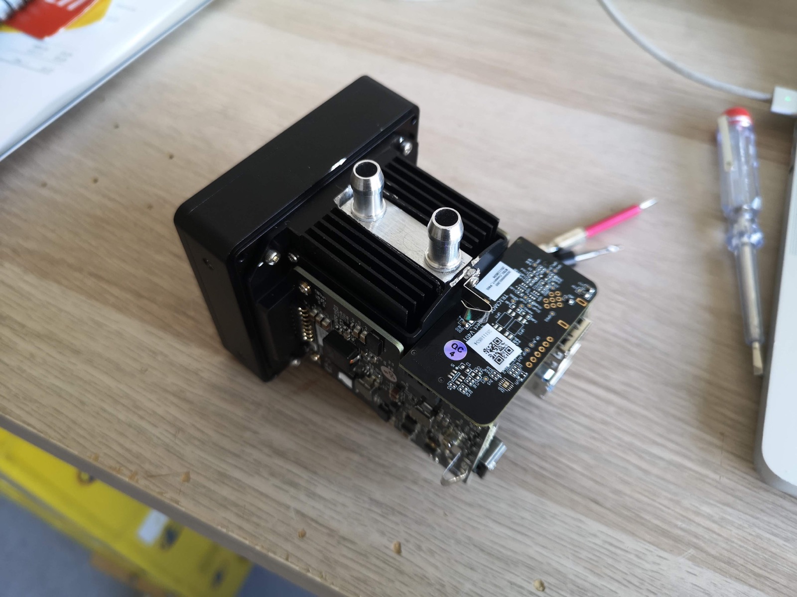 A small cooled CMOS camera on a wooden desk, its stock heat sink replaced by a machined aluminium water block with two metal hose fittings on top.