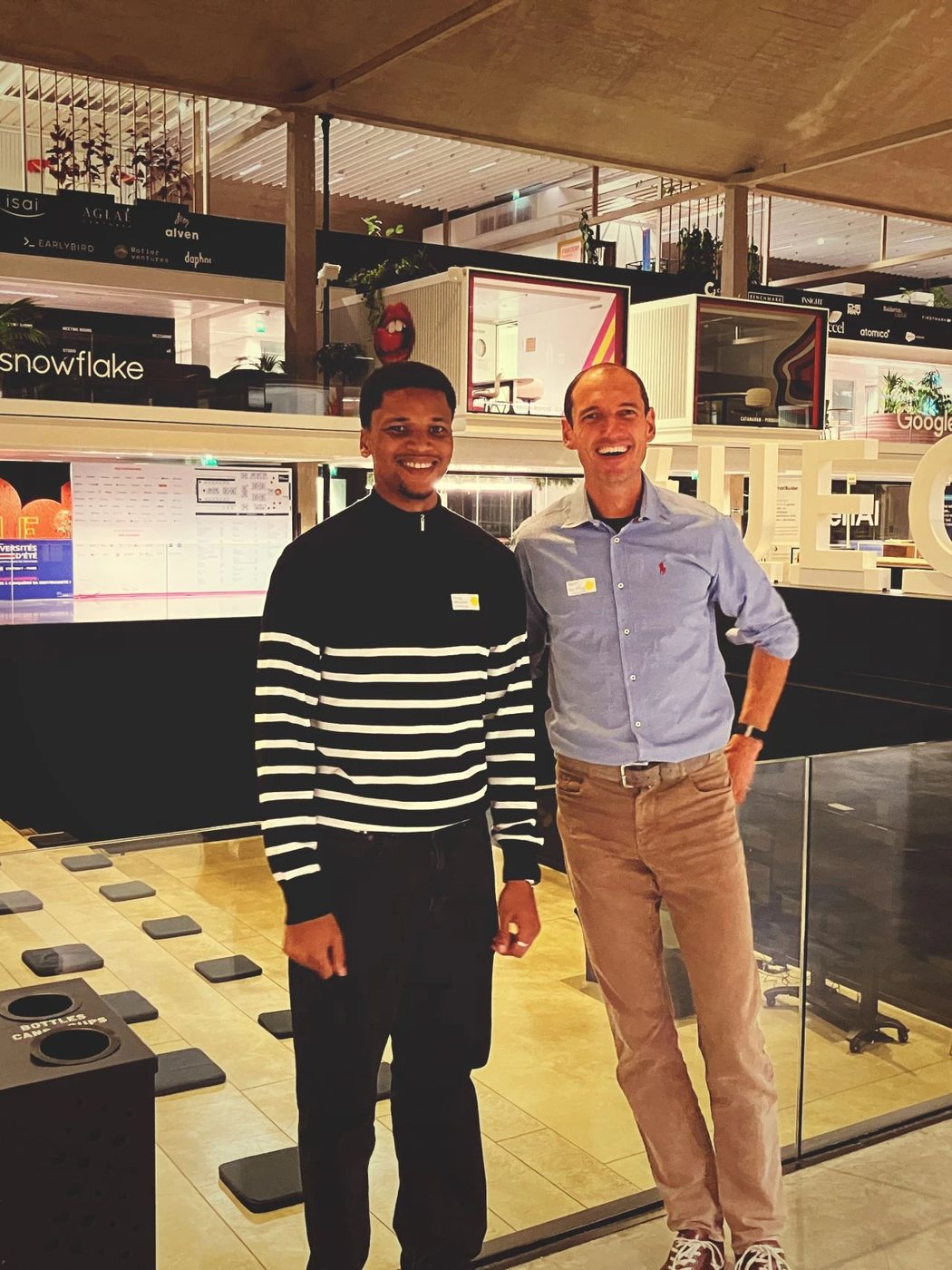 Peter Dike and Robin Wilkening standing side by side in the Station F atrium, name badges on, investor logos on the wall behind them.