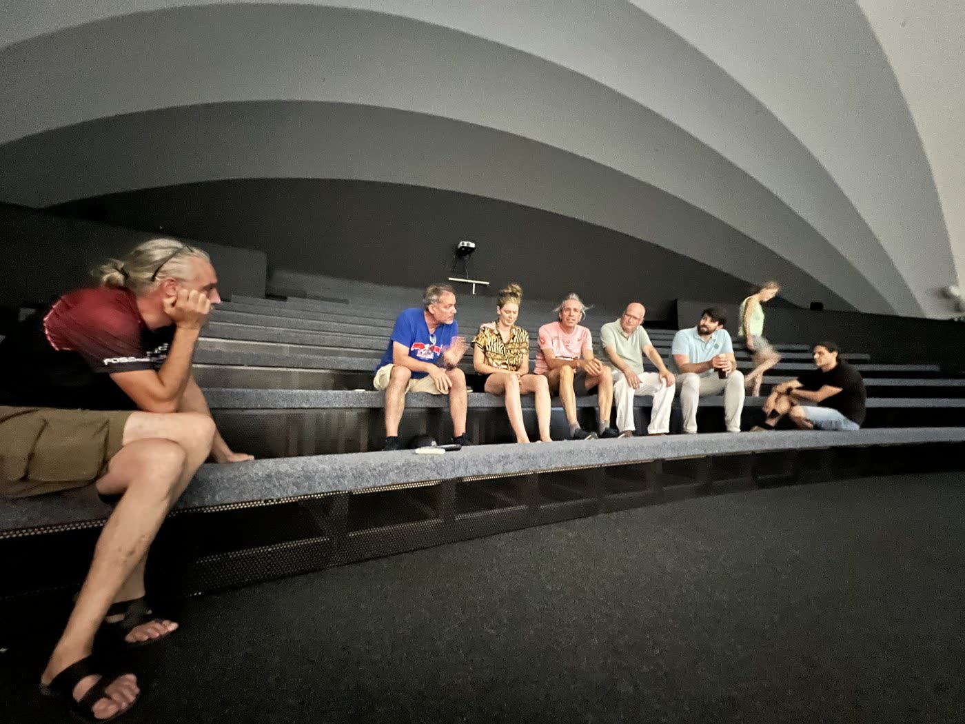 Participants sitting in a loose row on the tiered benches of the curved amphitheatre, mid-conversation.