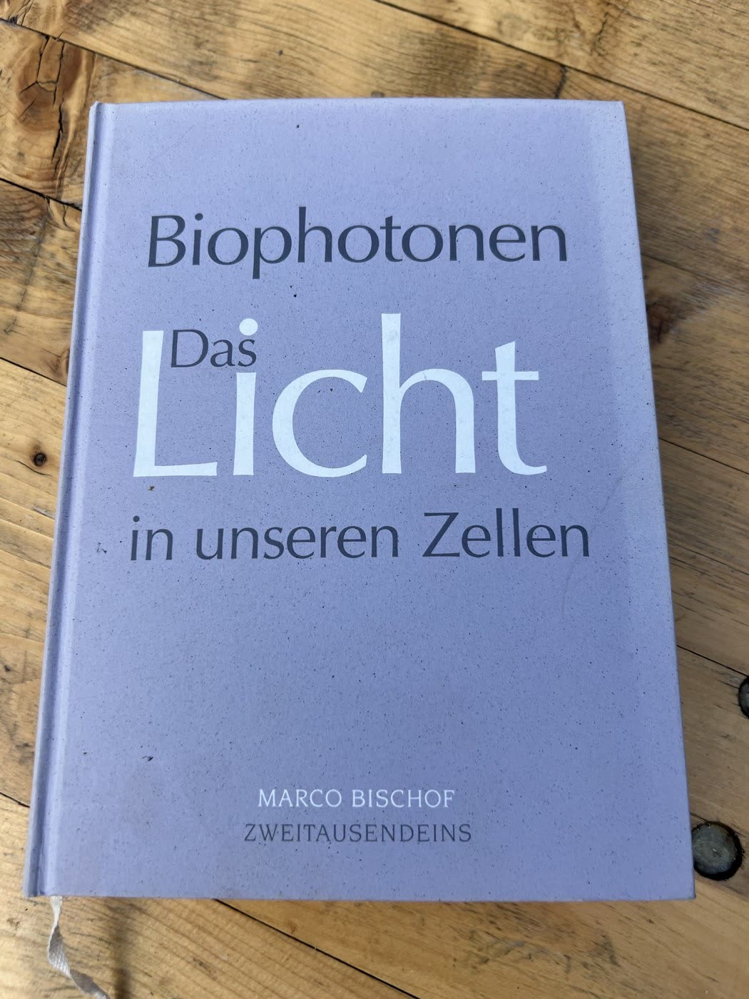 The cover of Marco Bischof's book Biophotonen: Das Licht in unseren Zellen, resting on a wooden table.