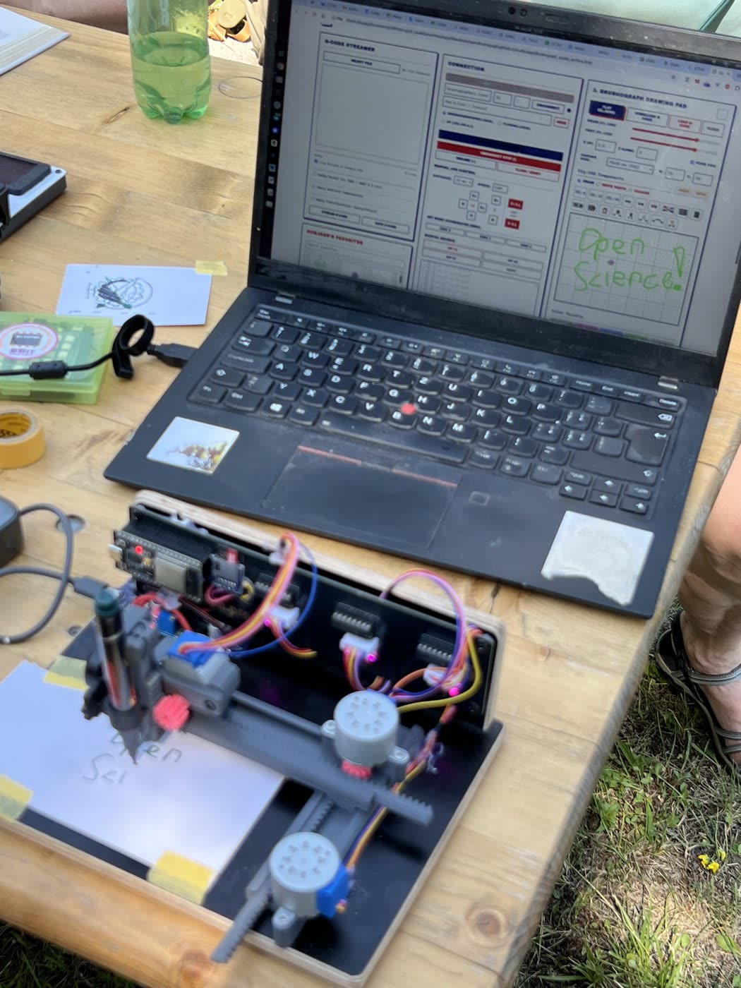 An open brushograph pen plotter beside a laptop whose screen reads 'Open Science'.