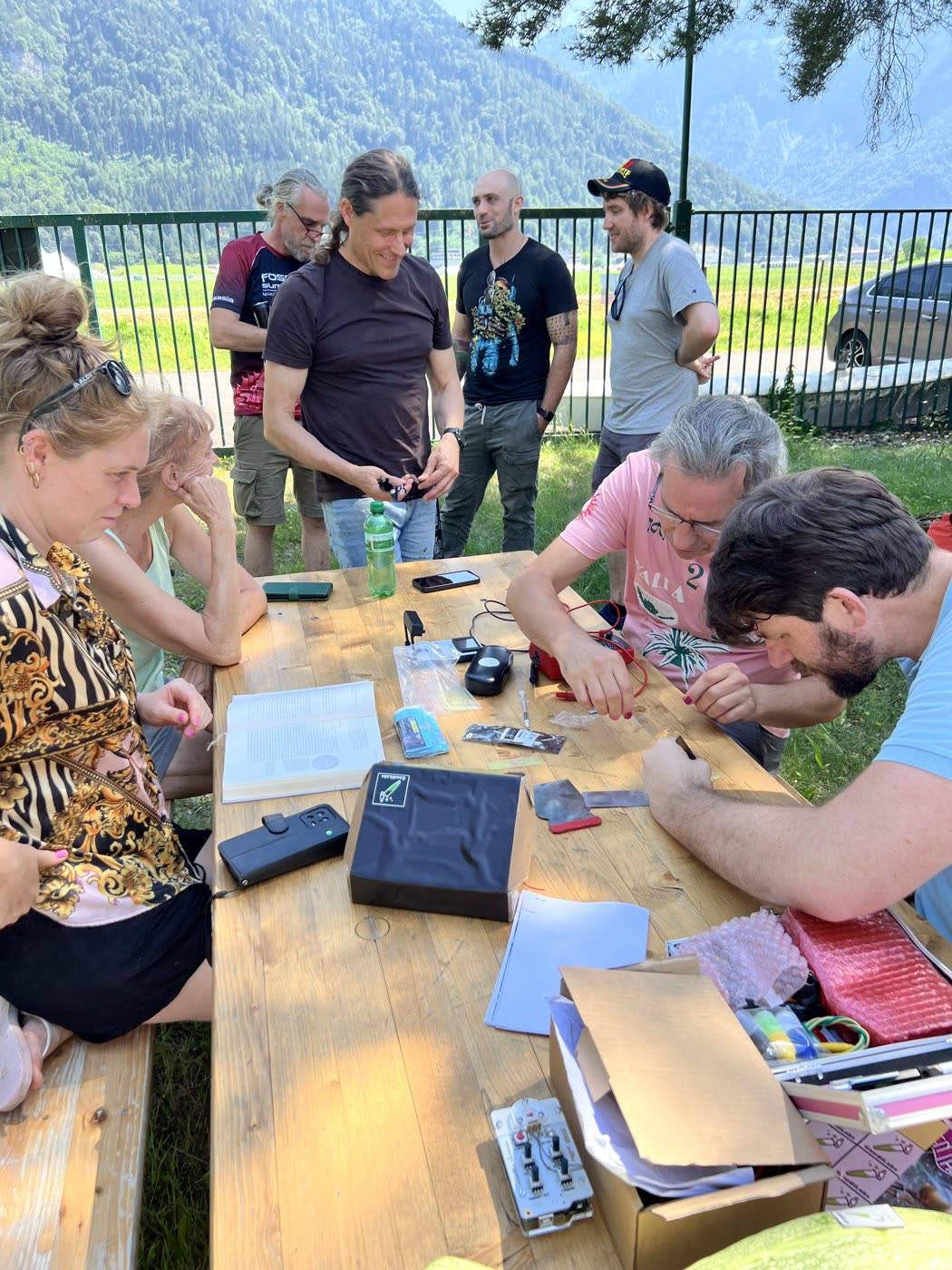 Open hardware kits, instruments, and laptops spread across a long table with participants gathered around it.